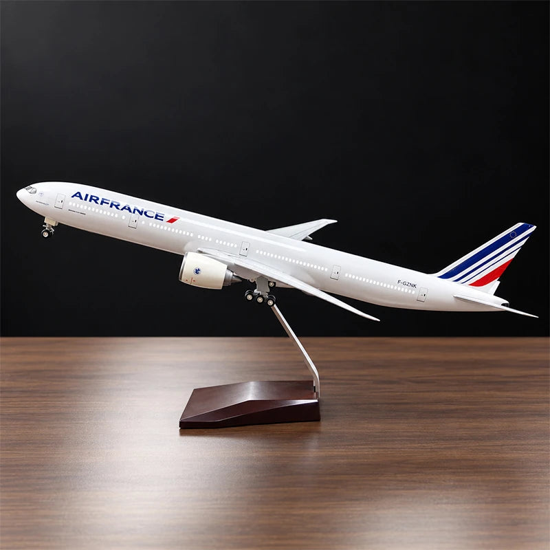 Air France Boeing 777-300ER 1:157 scale aircraft display model with LED cabin lighting, metal stand and wooden base, displayed on a living room table.
