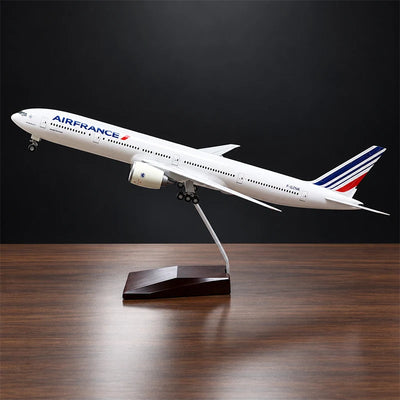 Air France Boeing 777-300ER 1:157 scale aircraft display model with LED cabin lighting, metal stand and wooden base, displayed on a living room table.
