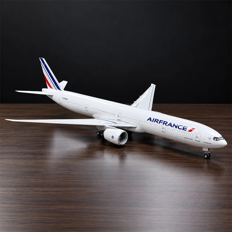 Air France Boeing 777-300ER 1:157 scale aircraft display model with LED cabin lighting, metal stand and wooden base, displayed on a living room table.